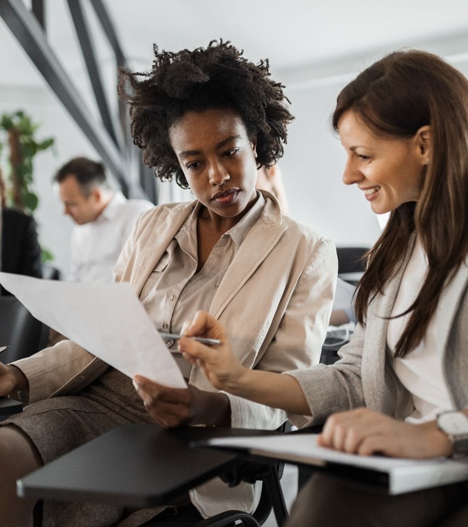two woman sitting next to each other talking about business with important documents